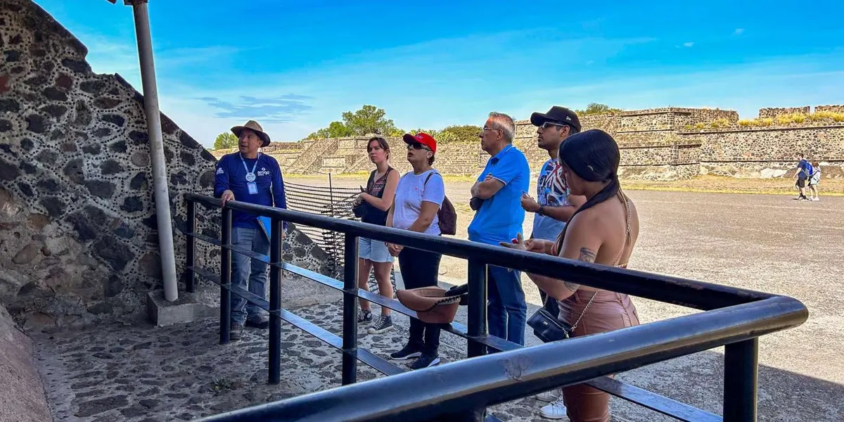 Guide and visitors beside stone carvings and a viewing rail